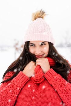 Winter season. Portrait of a beautiful smiling woman in red sweater and hat in snowy park