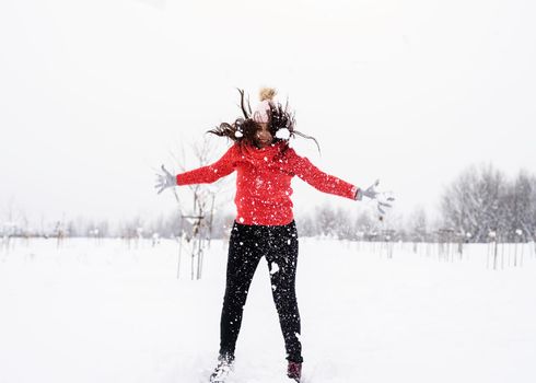 Winter fun. Young brunette carefree woman in red sweater jumping in snow outdoors