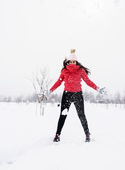 Winter fun. Young brunette carefree woman in red sweater jumping in snow outdoors