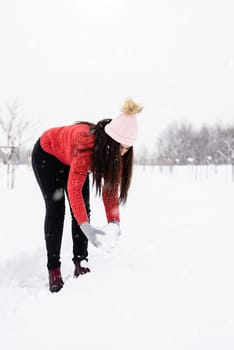 Winter season. Young brunette woman in red sweater playing with snow in park
