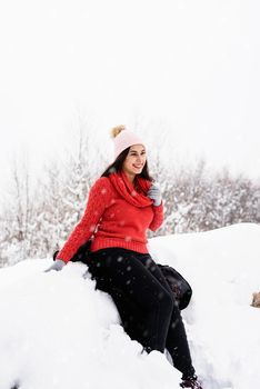 Winter season. Portrait of a beautiful smiling woman in red sweater and hat in snowy park