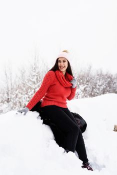 Winter season. Portrait of a beautiful smiling woman in red sweater and hat in snowy park