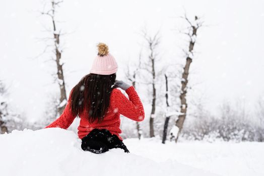 Winter season. Portrait of a beautiful smiling woman in red sweater and hat in snowy park