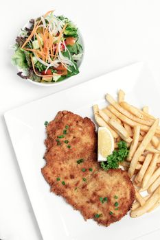 german breaded pork schnitzel with french fries on white studio background