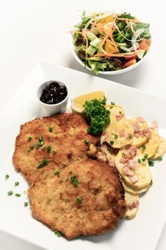 german breaded organic pork schnitzel with bacon fried potatoes cranberry sauce and salad on white studio background