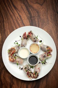 asian fresh vegetable vegan spring rolls with sauces on wood restaurant table background in vietnam