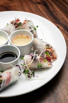 asian fresh vegetable vegan spring rolls with sauces on wood restaurant table background in vietnam