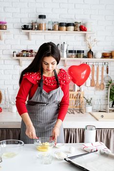 Valentines Day. Woman in red dress and gray apron making valentine cookies at the kitchen