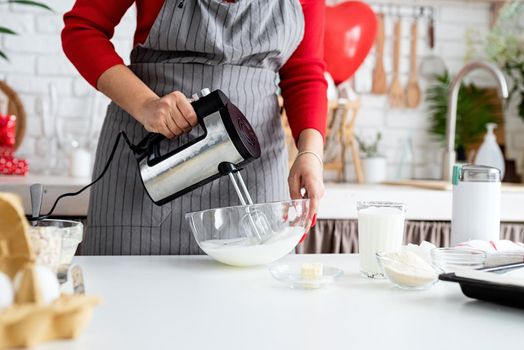 Valentines Day. Woman in red dress and gray apron making valentine cookies at the kitchen