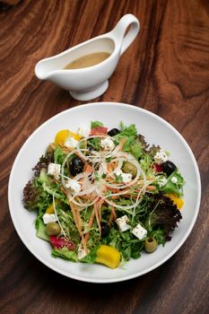 greek salad with feta cheese and olives with citrus vinaigrette on wooden table