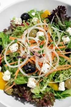 greek salad with feta cheese and olives with citrus vinaigrette on white table