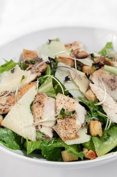 organic chicken caesar salad with parmesan cheese and croutons on white table background