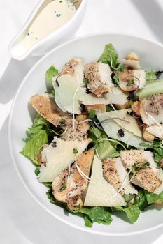 organic chicken caesar salad with parmesan cheese and croutons on white table background