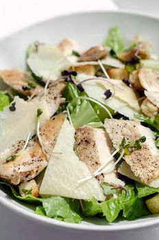 organic chicken caesar salad with parmesan cheese and croutons on white table background