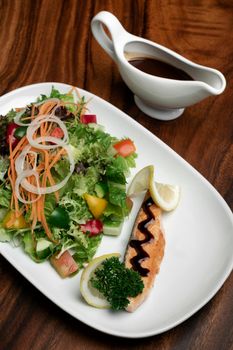 organic mixed vegetable salad with salmon fillet and balsamic vinaigrette on wood restaurant table