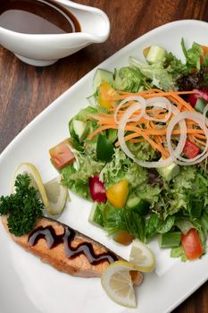 organic mixed vegetable salad with salmon fillet and balsamic vinaigrette on wood restaurant table