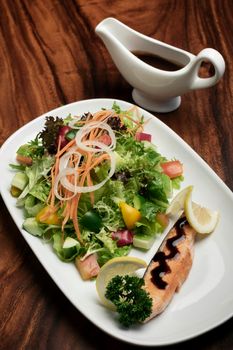 organic mixed vegetable salad with salmon fillet and balsamic vinaigrette on wood restaurant table