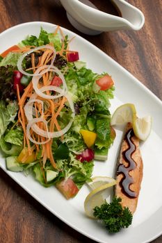 organic mixed vegetable salad with salmon fillet and balsamic vinaigrette on wood restaurant table