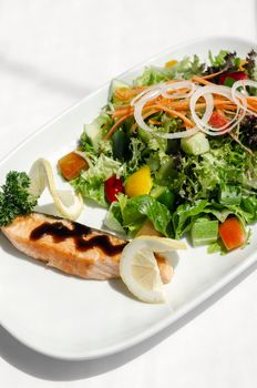 organic mixed vegetable salad with salmon fillet and balsamic vinaigrette on white restaurant table