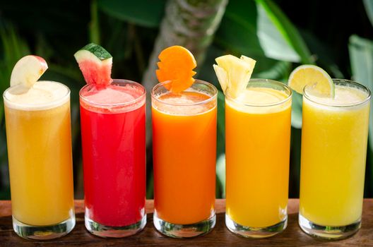 mixed fresh organic fruit juice glasses selection on sunny garden table