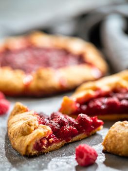 Slice of perfect raspberry galette. Delicious rustic homemade tart with frozen or fresh raspberries on gray background. Beautiful piece of galette with raspberries, copy space. Vertical