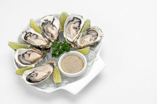 Six fresh oysters with lime wedges and citrus vinaigrette sauce