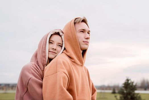 Happy young loving couple wearing hoods embracing each other outdoors in the park