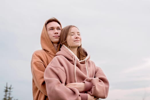 Happy young loving couple wearing hoods embracing each other outdoors in the park