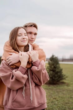 Happy young loving couple wearing hoods embracing each other outdoors in the park