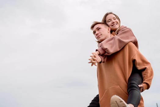 Happy young loving couple wearing hoods embracing each other outdoors in the park having fun on sky background