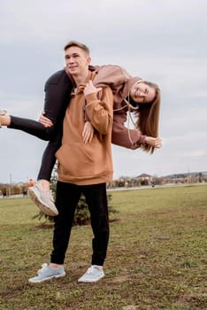 Happy young loving couple wearing hoods embracing each other outdoors in the park having fun