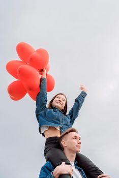 Valentines Day. Young loving couple hugging and holding red heart shaped balloons outdoors