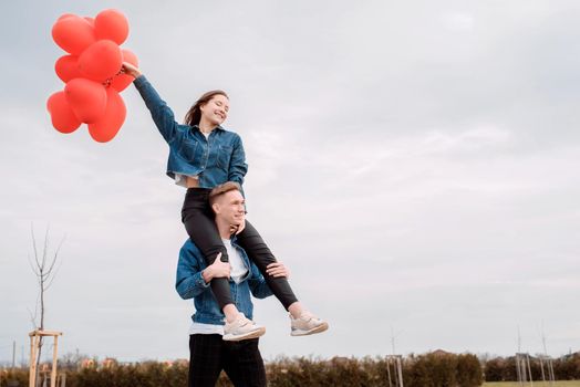 Valentines Day. Young loving couple hugging and holding red heart shaped balloons outdoors