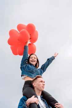 Valentines Day. Young loving couple hugging and holding red heart shaped balloons outdoors