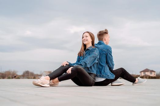 Young loving couple wearing jeans sitting back to back in the street spending time together