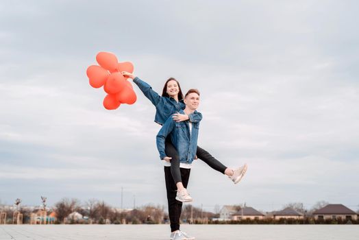 Valentines Day. Young loving couple hugging and holding red heart shaped balloons outdoors