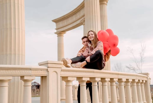 Happy young loving couple embracing each other outdoors in the park having fun holding red balloons