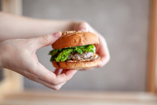 A woman holds a sandwich with a cutlet, cheese and green salad. Sandwich at home. The concept of healthy and unhealthy food.