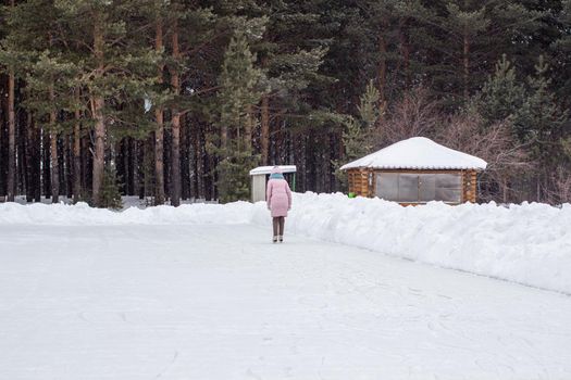 One girl in warm clothes rides on an ice rink near the forest. Winter sports recreation. Entertainment in quarantine