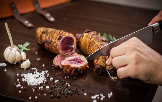 slicing a serving of organic roast beef roll with knife on wood table with garlic pepper and salt in melbourne australia