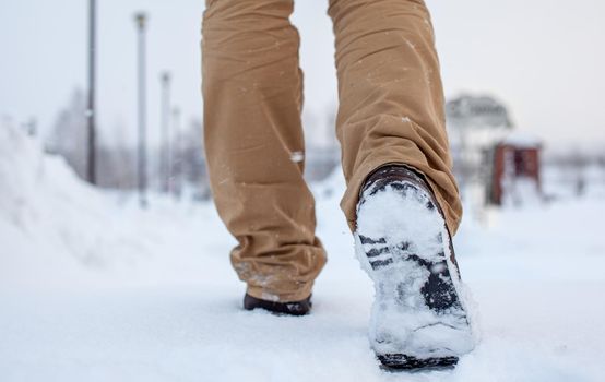 A person is walking on a slippery road, the first snow in the park, winter shoes, the road is covered with slippery ice and white snow. Footprints and shoes close-up.