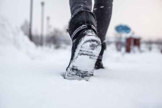 A person is walking on a slippery road, the first snow in the park, winter shoes, the road is covered with slippery ice and white snow. Footprints and shoes close-up.