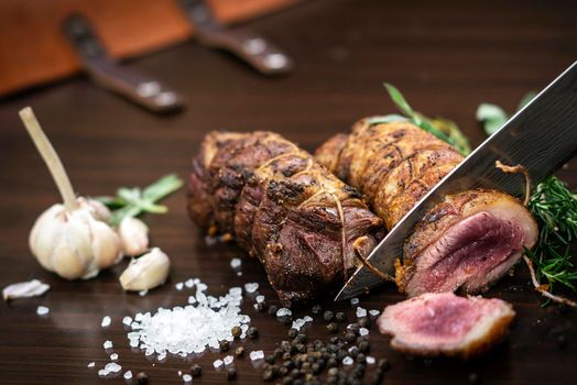 slicing a serving of organic roast beef roll with knife on wood table with garlic pepper and salt in melbourne australia