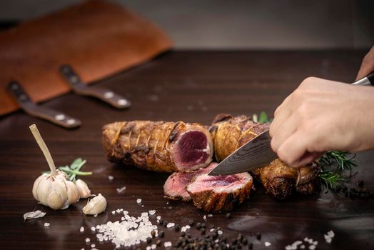 slicing a serving of organic roast beef roll with knife on wood table with garlic pepper and salt in melbourne australia