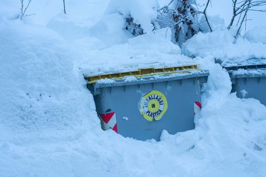 a bin for the separate collection of paper buried by the snow at the edge of a road