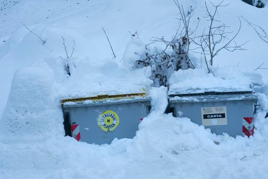 a bin for the separate collection of paper buried by the snow at the edge of a road