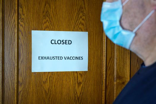 A man in front of  a closed door with a sign that reads Closed because the vaccine is out of stock