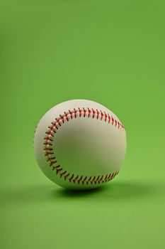 Close up one new baseball ball with red stitch over green background, low angle view