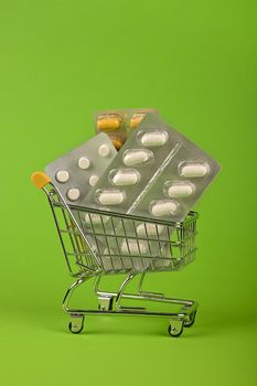 Close up several different blister packs of pills in small shopping cart over green background, concept of online medicine order delivery, low angle view