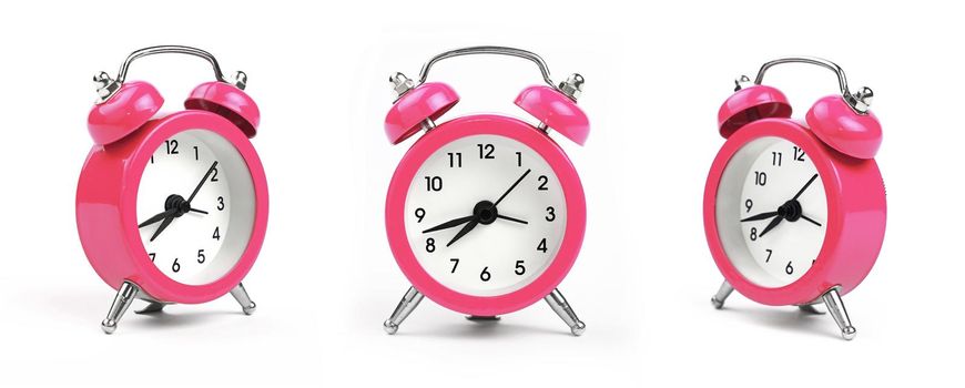 Three small pink metal alarm clock with red bells over white background, close up, low angle view in different perspectives